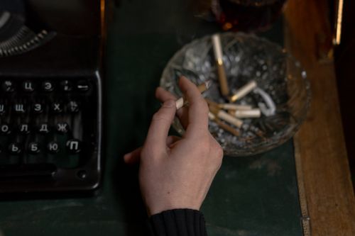 Free Close-up of a hand holding a cigarette near a vintage typewriter and ashtray, evoking creative inspiration. Stock Photo