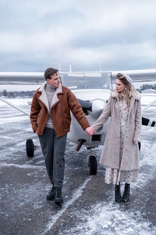 Young couple in warm clothes holding hands on airfield