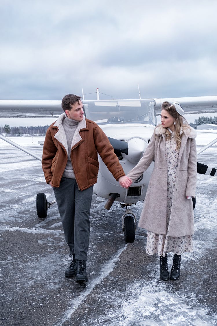 Young Couple In Warm Clothes Holding Hands On Airfield