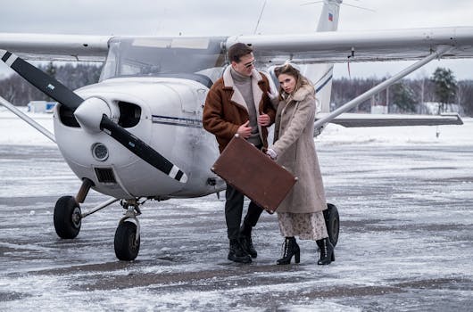 A fashionable couple stands by a small aircraft on a snowy airfield, highlighting winter travel.
