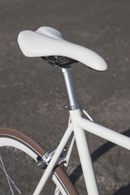 A detailed view of a white bicycle saddle on an asphalt background, showcasing modern design.