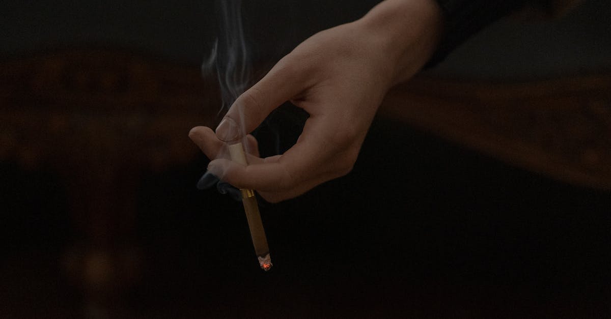 A hand holding a lit cigarette over an ashtray indoors, representing smoking habits.
