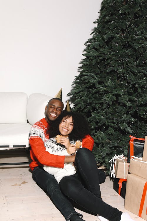 A Happy Couple Sitting Beside A Christmas Tree