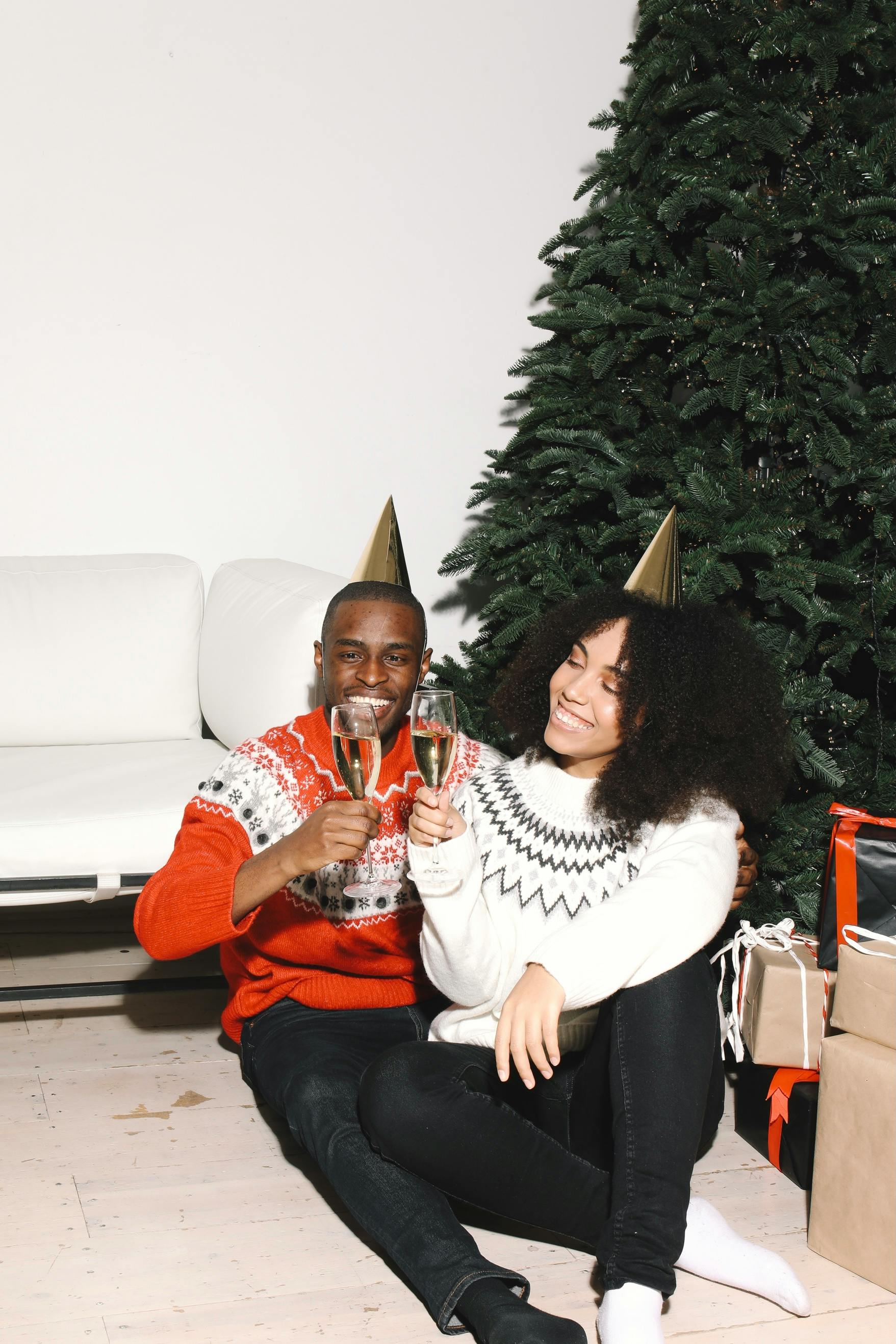 Happy couple in holiday sweaters celebrating Christmas with champagne by the tree.