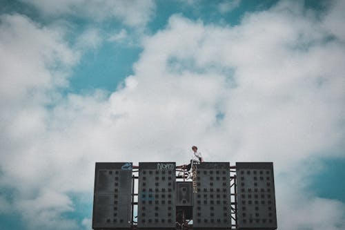 Man in White Shirt and Black Pants Sitting on Building Under Blue Sky