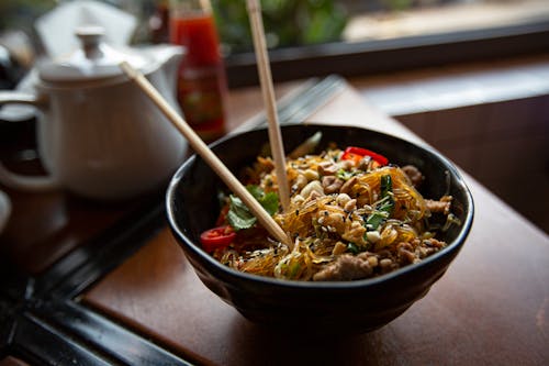 Bowl of delicious noodles with meat and vegetables served on table