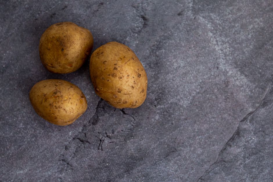 Several small brown baby potatoes arranged on a dark gray surface`