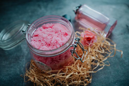Free From above of pink body scrub in glass jar placed on table with perfume bottle and pile of shredded paper Stock Photo