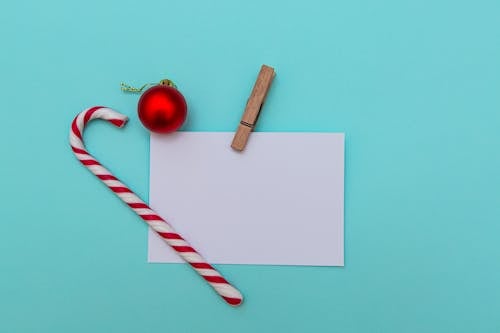 Top view of Christmas candy cane and red bauble on blue table composed with blank paper greeting card pinned with wooden clip