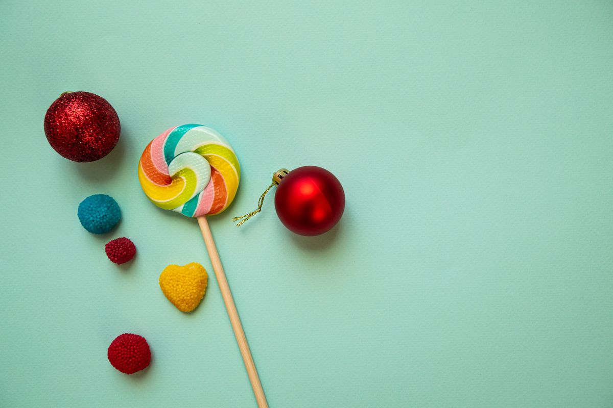 From above of colorful lollipop on wooden stick placed on green background white shiny red baubles and various decorative elements