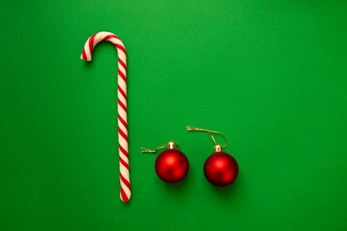 Top view pair of red shiny Christmas balls composed with candy cane on green background