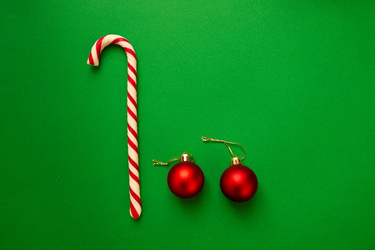 Striped Christmas Candy Cane And Red Baubles Placed On Green Table