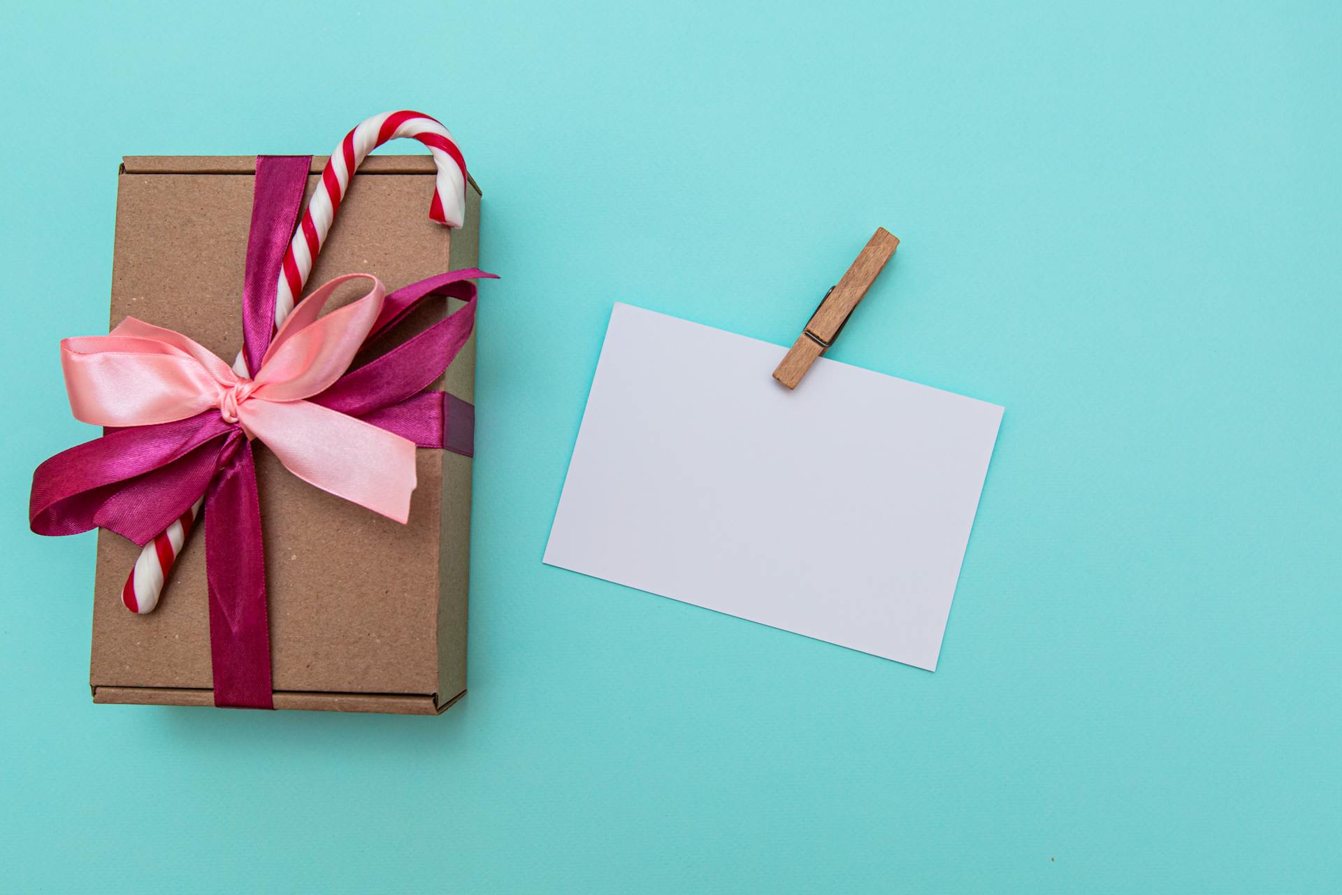 Top view of a gift box with candy cane and blank card on blue background, perfect for holiday themes.