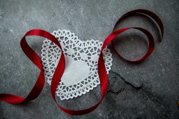 Heart Shaped Paper Doily And Red Ribbon On Table