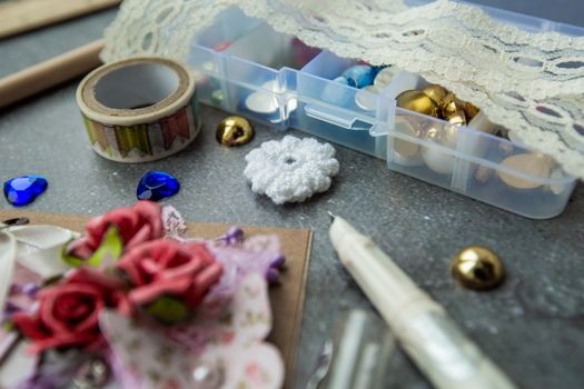 High angle of assorted beads and fancy stones in plastic container placed on table with various tools for handmade craft