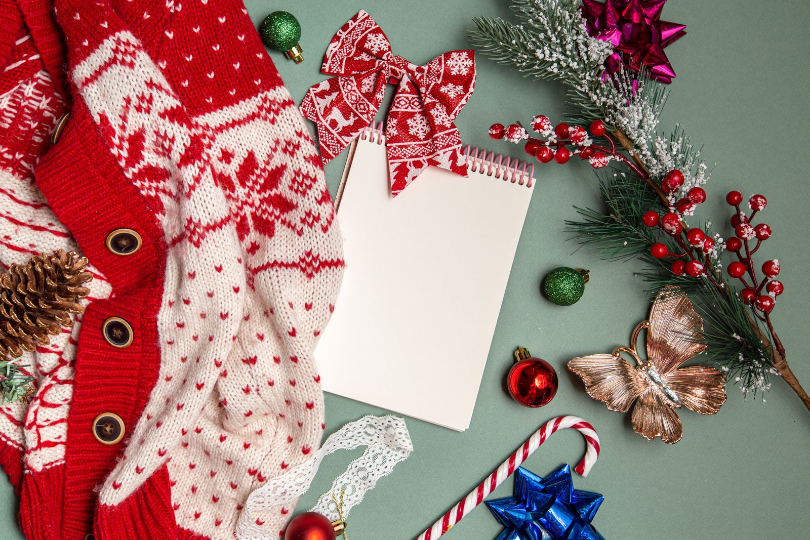 Blank spiral notebook arranged with Christmas decorations on a green surface.