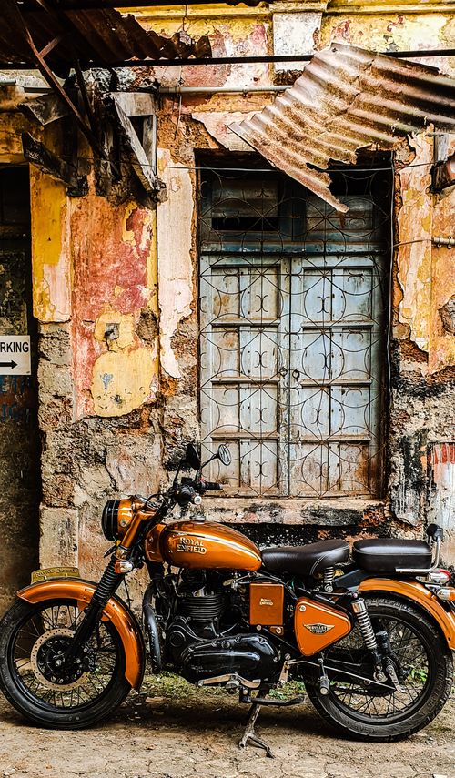 Free Orange motorcycle parked by a rustic, decaying wall in Panaji, Goa, India. Stock Photo