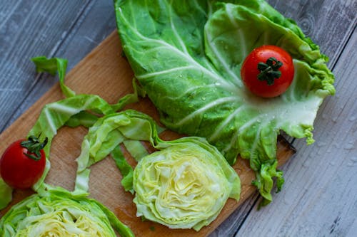 Top view of fresh chopped green cabbage and tomatoes with water drops placed on wooden cutting board in kitchen