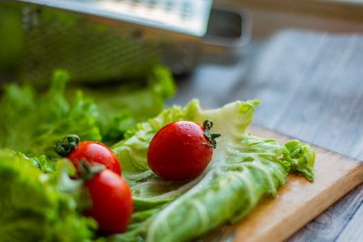 Closeup of fresh washed red tomatoes and green cabbage leaves placed on wooden cutting board near grater in kitchen