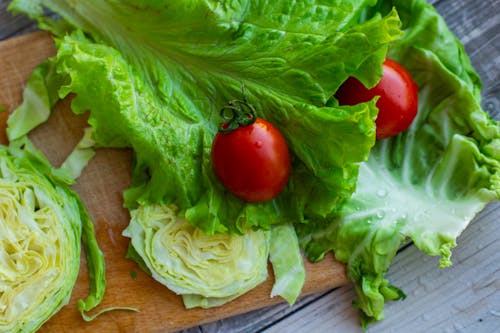 Free From above of assorted leaf and iceberg lettuce with ripe tomatoes arranged on wooden chopping board in kitchen in sunlight Stock Photo