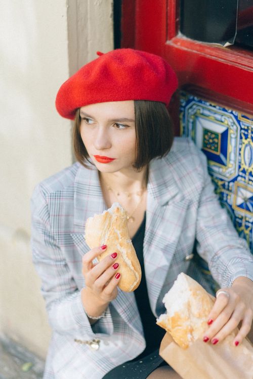 Free Chic young woman in red beret enjoys baguette outdoors, capturing Parisian style. Stock Photo