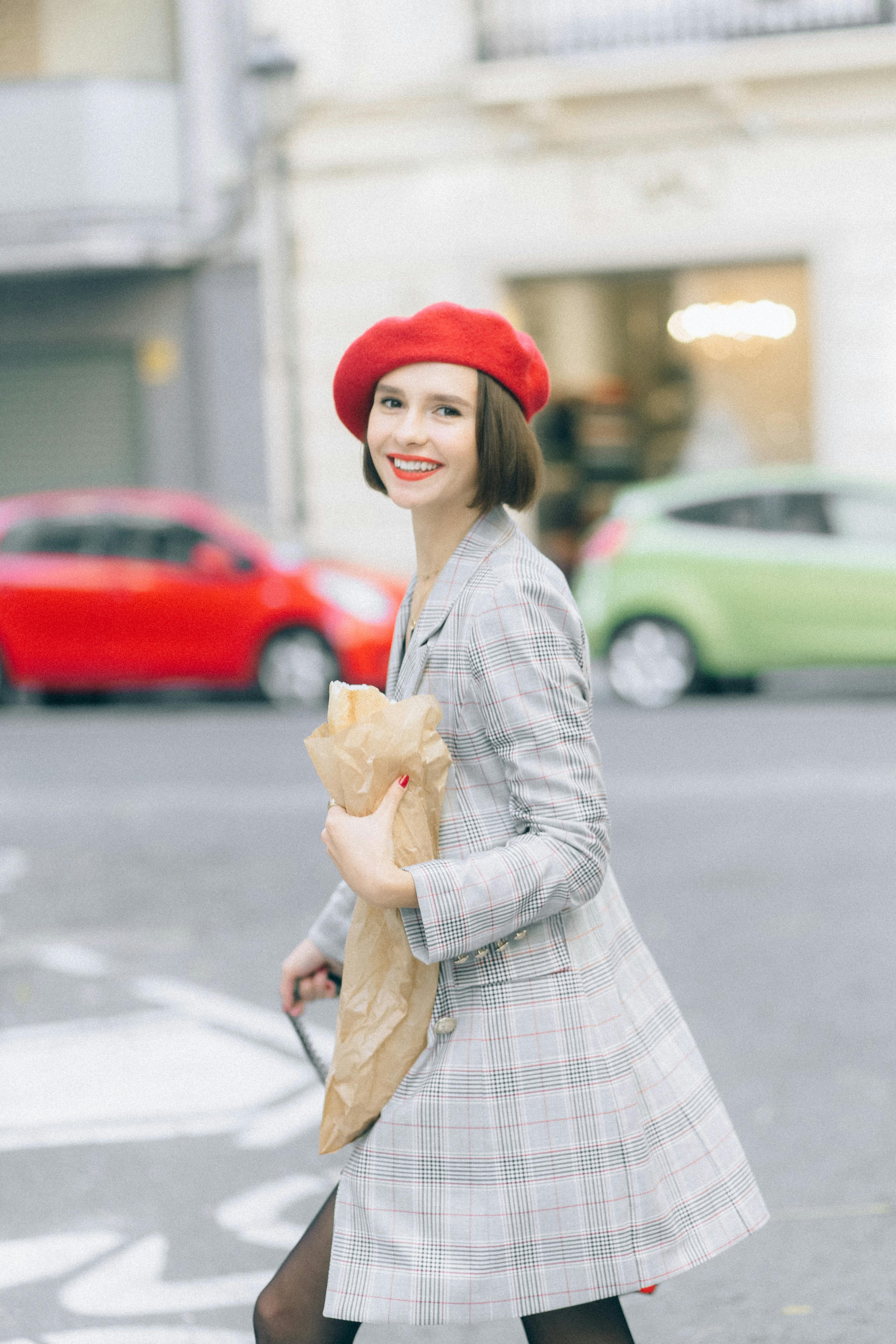 Stylish woman in red beret smiling while walking in urban setting.