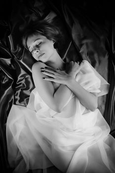 Black and white top view of young dreamy female lying on smooth creased textile