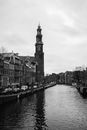 Black and white of traditional houses and Westerkerk Parish church located on canal shore against cloudy sky in Amsterdam