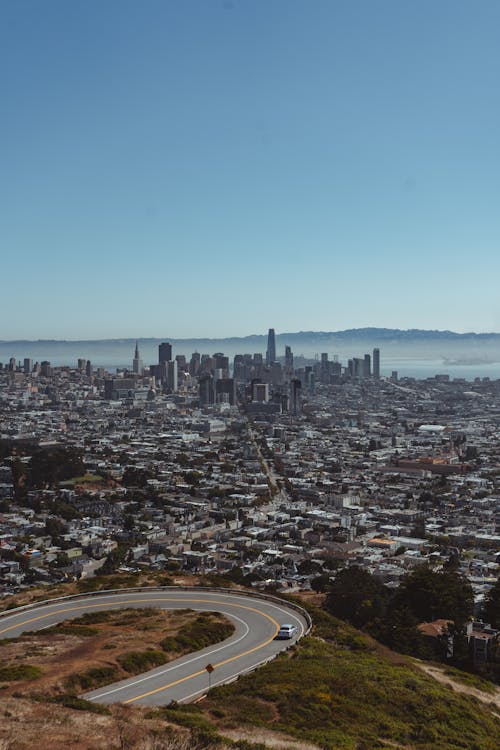 Free Picturesque scenery of curvy asphalt road going through hilly terrain above San Francisco City with modern skyscrapers against cloudless blue sky Stock Photo