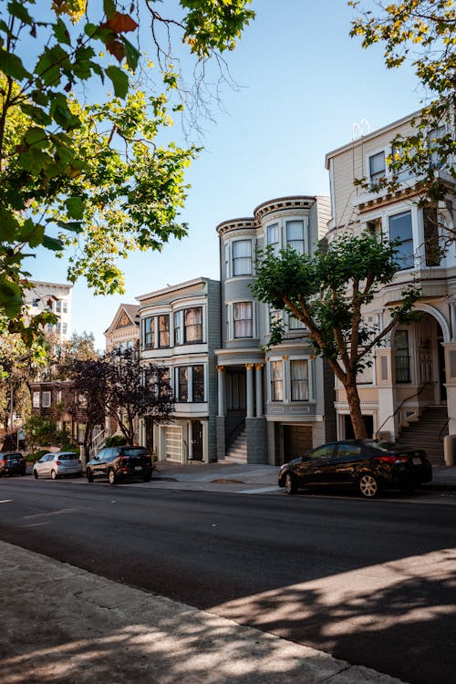 Various cars parked on asphalt road near classic styled residential houses against cloudless blue sky in San Francisco