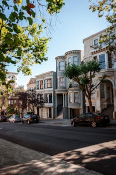 Various cars parked on asphalt road near classic styled residential houses against cloudless blue sky in San Francisco