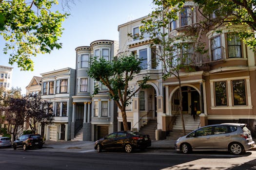 Charming Victorian houses on a sunny San Francisco street lined with trees and parked cars.