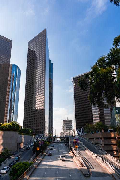 Contemporary skyscrapers with glass mirrored facades located near road against blue sky in Los Angeles