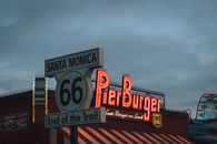 Low angle of road sign with Route 66 End of the Trail inscription located near fast food restaurant against cloudy evening sky on Santa Monica Beach