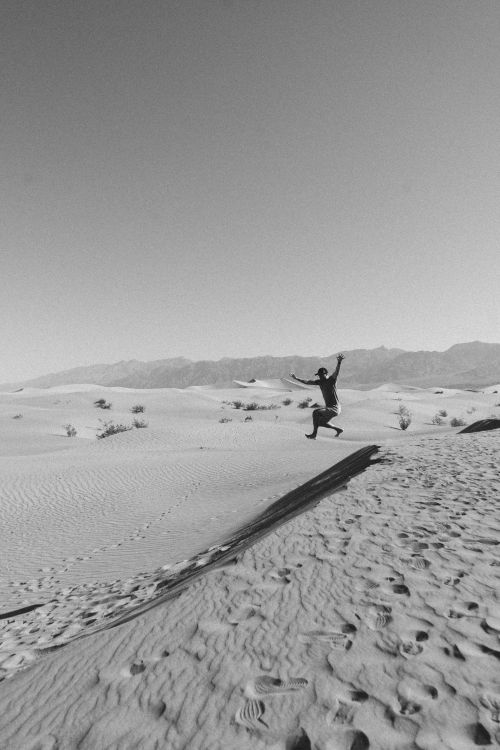 Free Black and white of unrecognizable male traveler jumping from sandy dune while having fun in desert on sunny day Stock Photo
