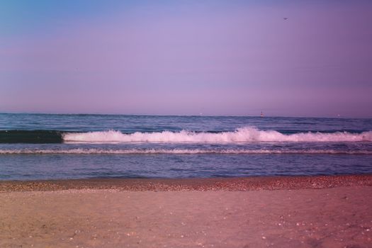 Serene beach with gentle waves under a pink sunrise, capturing nature's tranquil beauty.