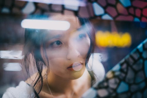 Gentle young Asian woman looking through window