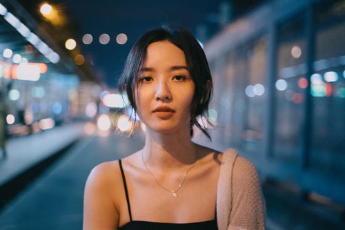 Free Slim ethnic female looking at camera on blurred background of urban illumination on street Stock Photo