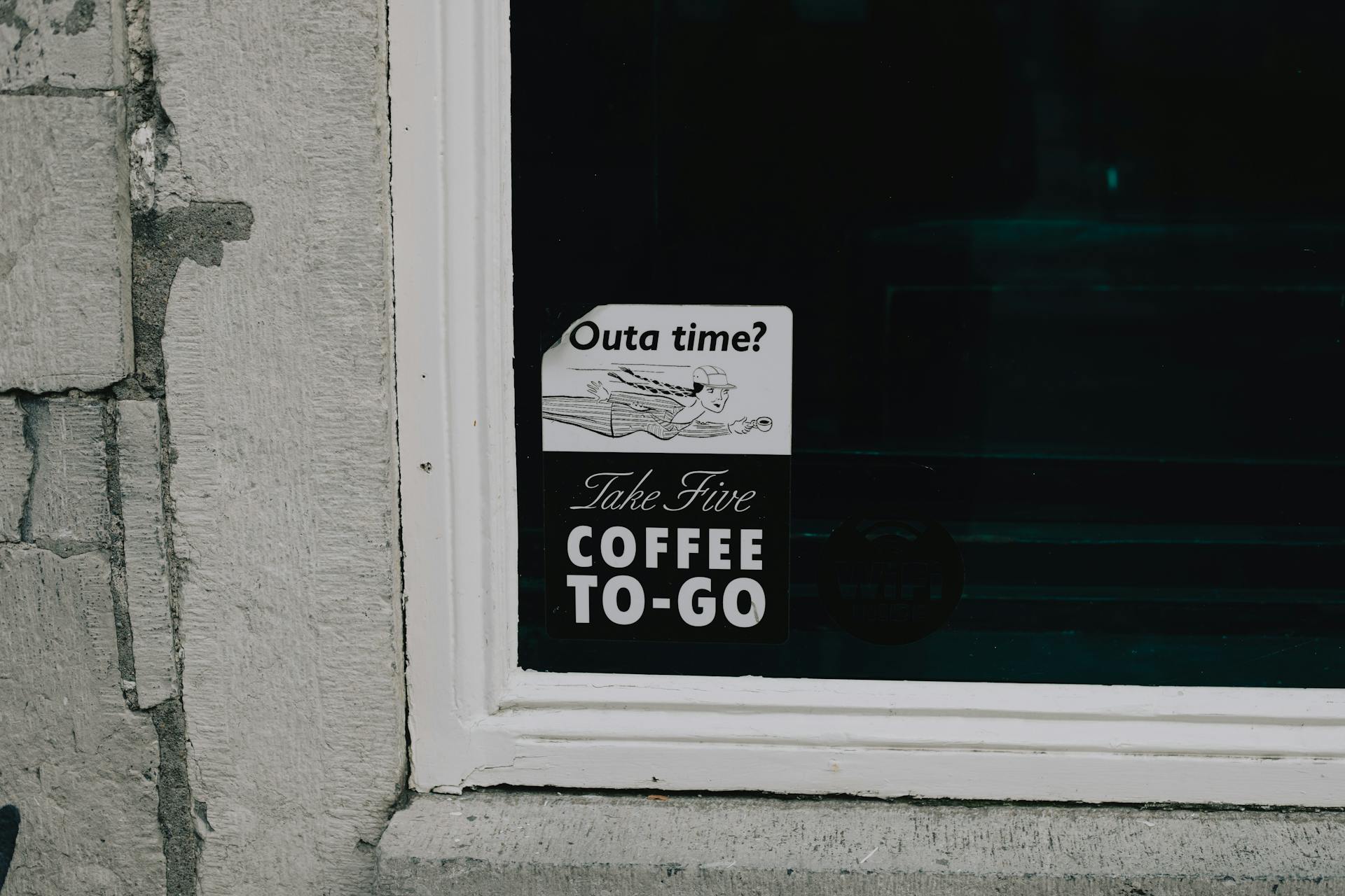 Exterior view of a 'Take Five Coffee To-Go' sign on a storefront window in Maastricht, Netherlands.