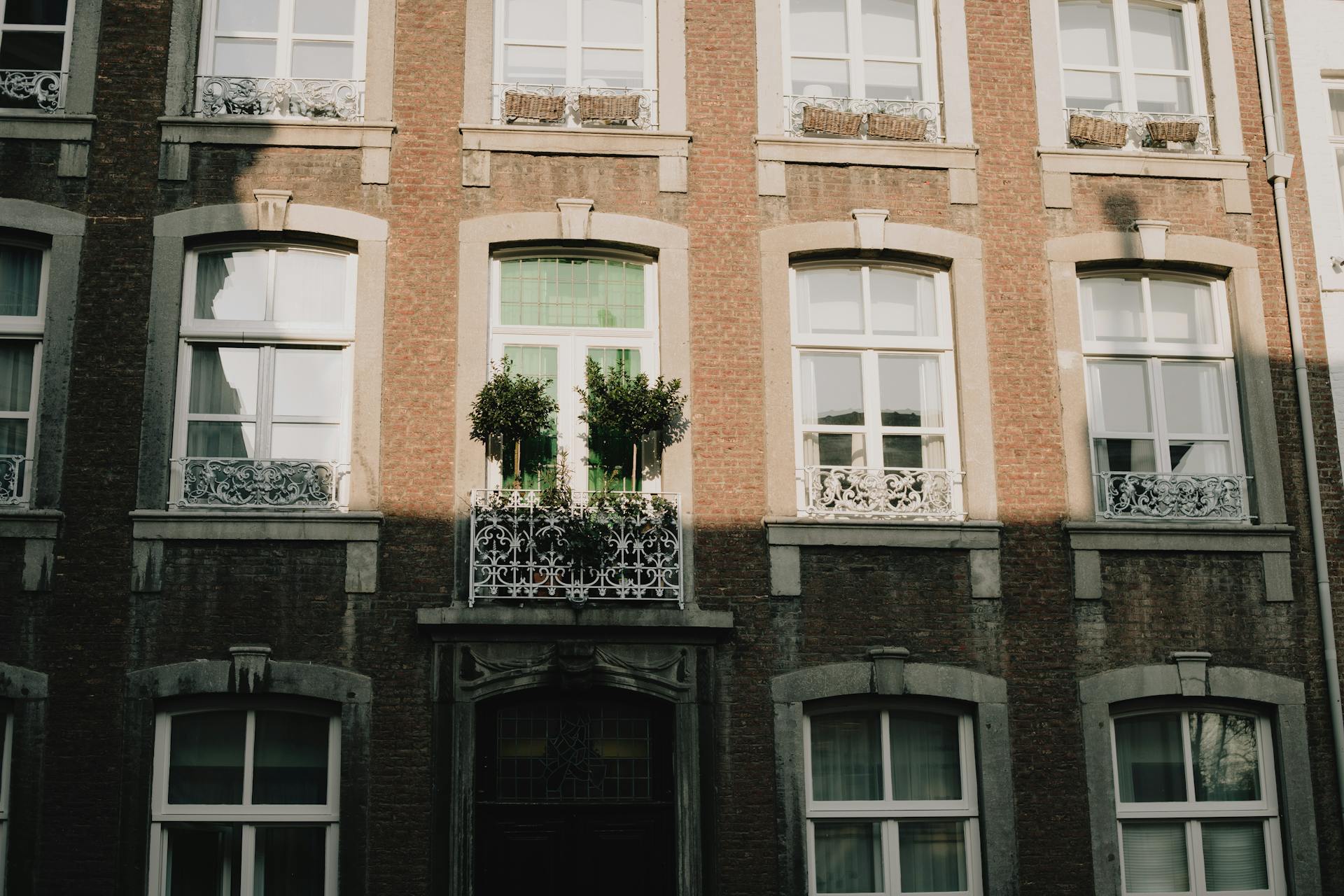 Elegant Maastricht building facade with intricate ironwork and lush greenery under natural light.