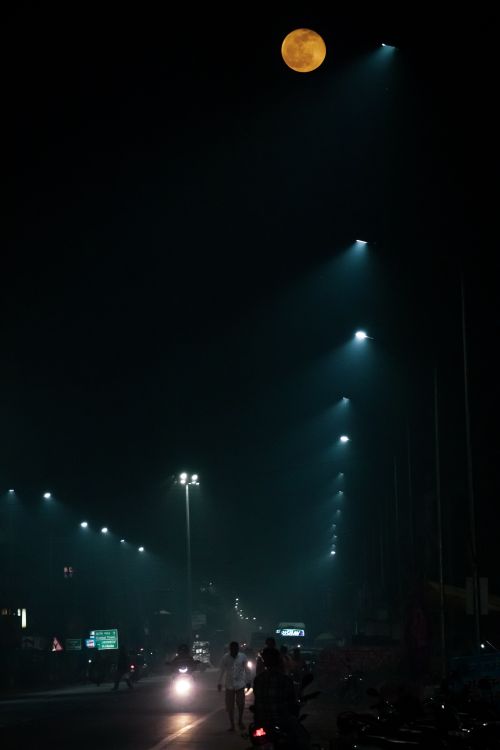 Free Unrecognizable people walking along illuminated street near driving vehicles against dark night sky Stock Photo