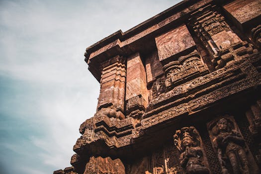 From below of ornamental carvings and sculptures of stone wall of ancient Konark Sun Temple located in India against cloudy sky