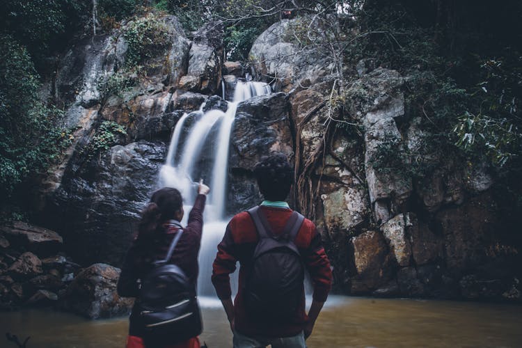 Anonymous Couple Standing Near Waterfall During Hiking Trip In Forest