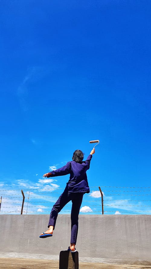 A Person Holding a Paint Roller under a Clear Blue Sky