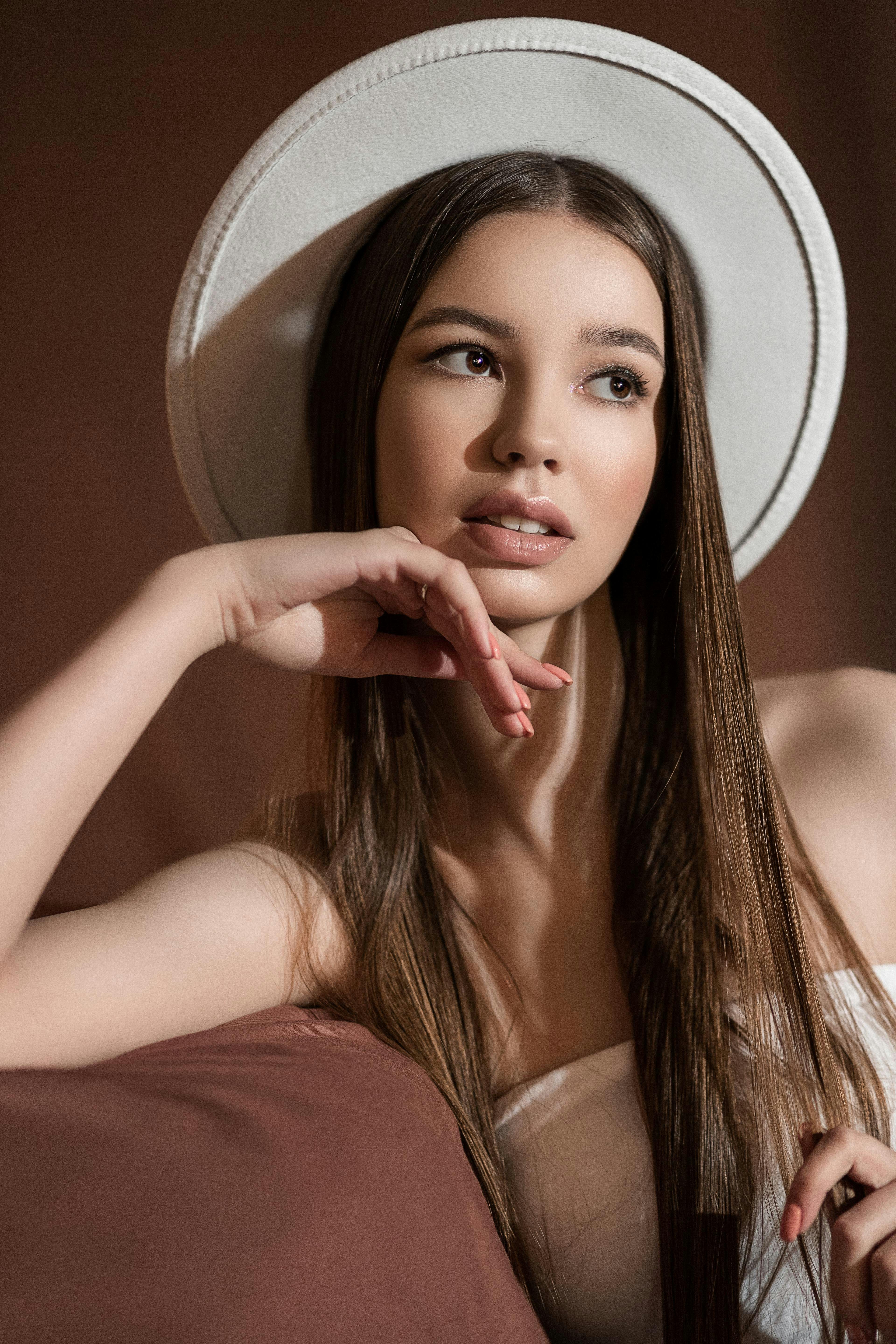 charming teenager in hat resting on sofa on brown background