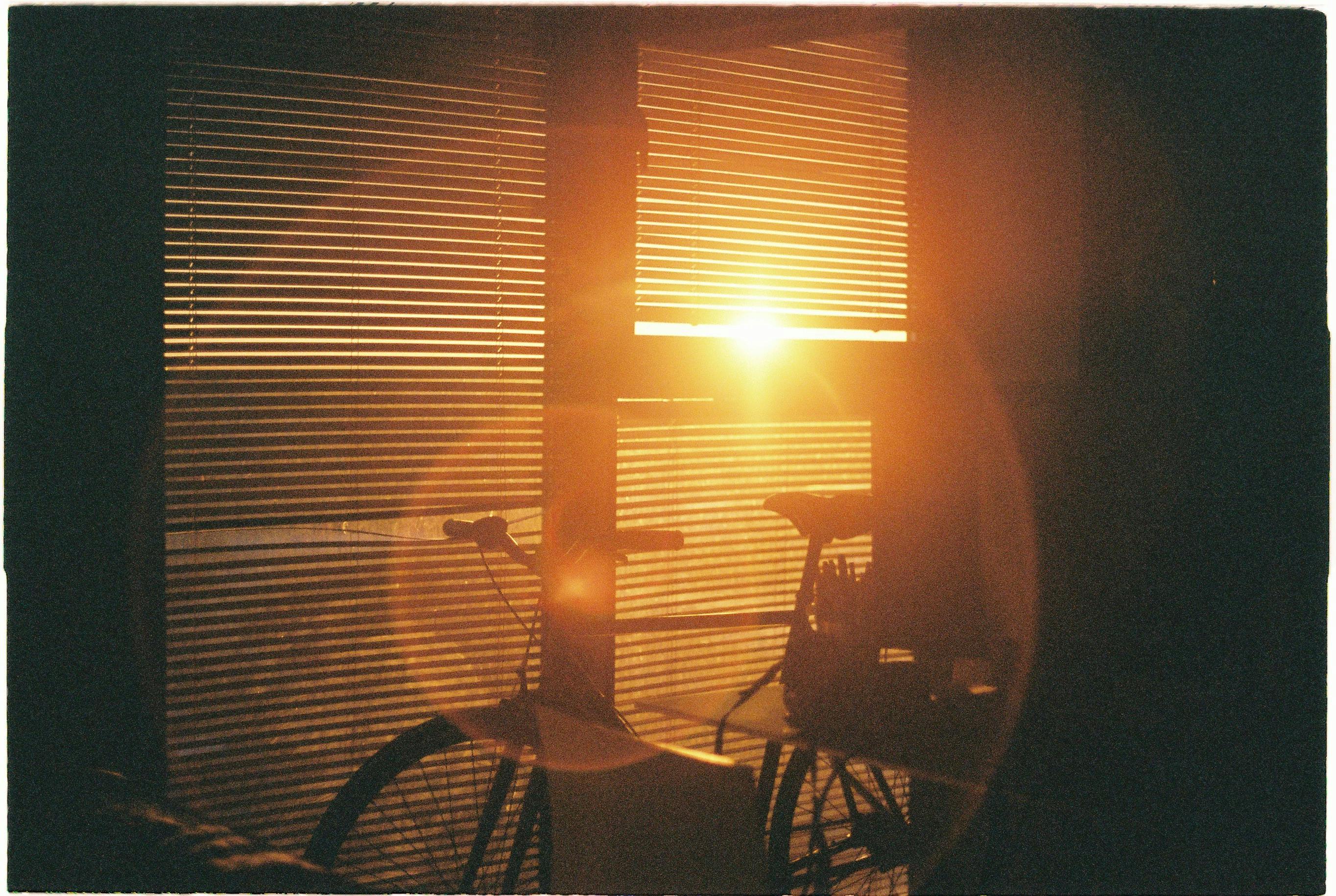 Golden sunlight streaming through window blinds, casting a silhouette of a bicycle. Captivating sunset scene.