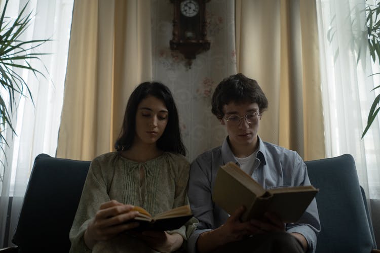 Man And Woman Sitting On A Blue Couch While Reading Books 