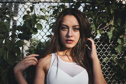 Elegant young woman posing outdoors against a leafy fence.