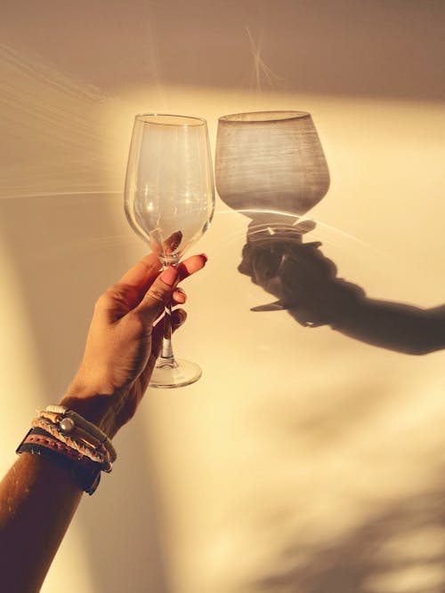 Crop woman with shiny glass against wall with shadow