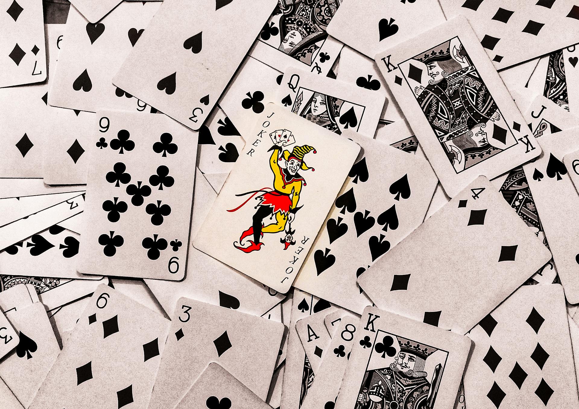 A vibrant joker card stands out in a scattered deck of monochrome playing cards.